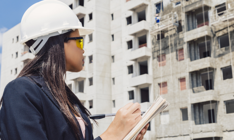 afro-americaine-en-casque-de-securite-ecrit-dans-le-bloc-notes-pres-du-batiment-en-construction